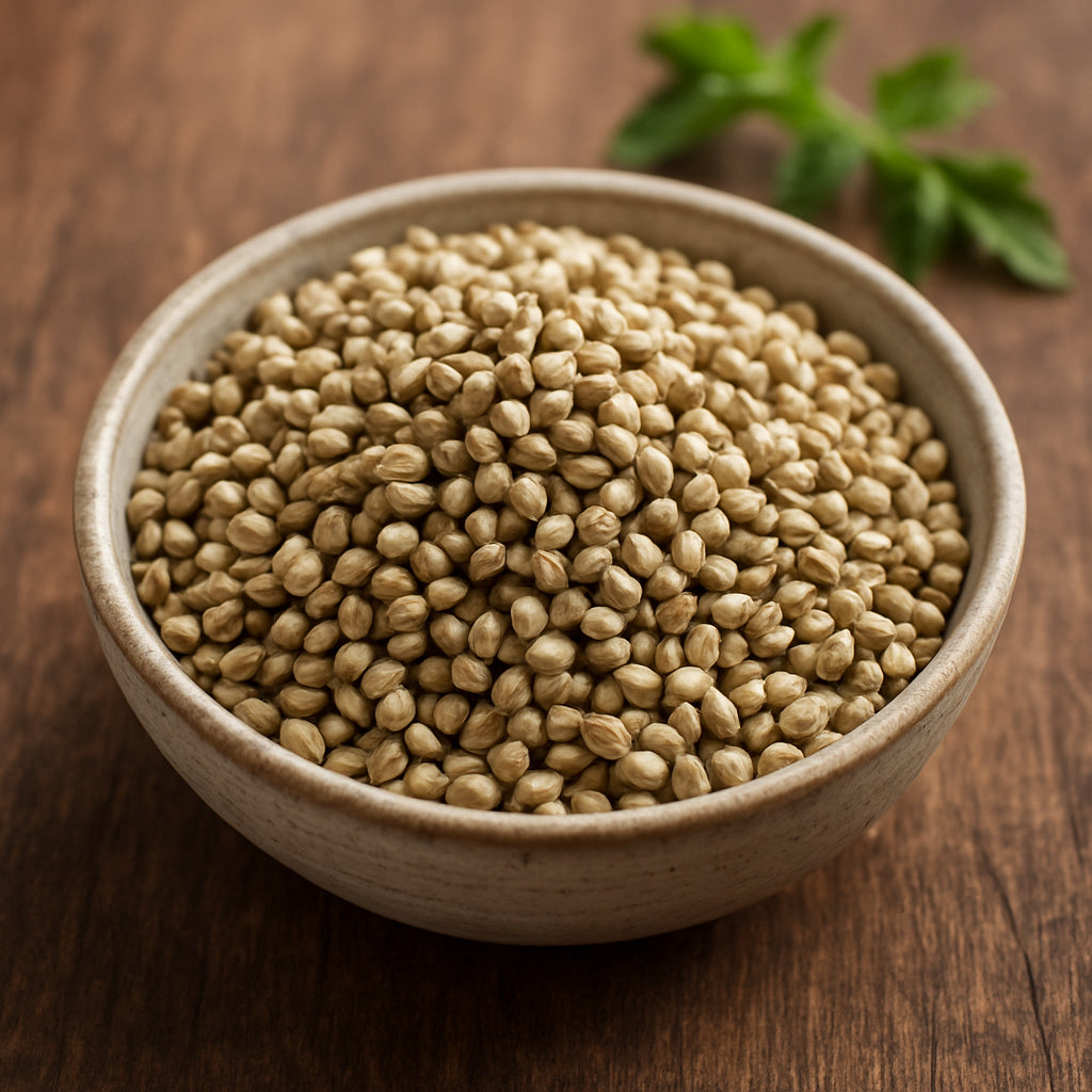 A realistic photo of a close‑up shot of hemp seeds arranged in a small bowl on a wooden table, with a subtle splash of green herbs in the background, showcasing their natural texture and earthy color. Alt: hemp seeds bowl with herbs.