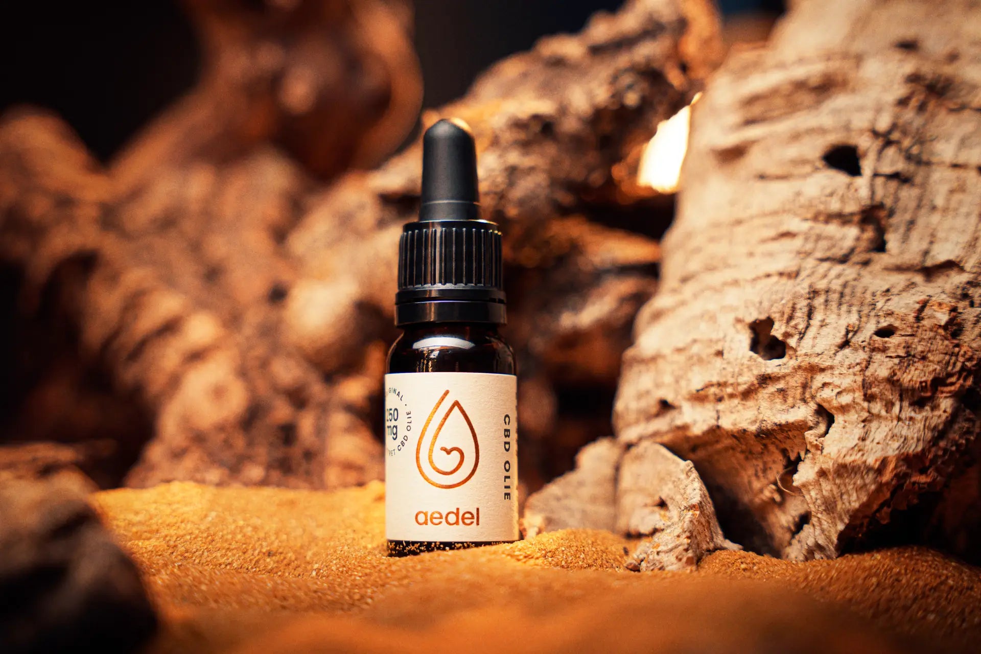 Aedel CBD Olie 250mg flaske placeret i naturligt sand og bark – symboliserer jordnær renhed, økologisk oprindelse og fuldspektret CBD kvalitet.