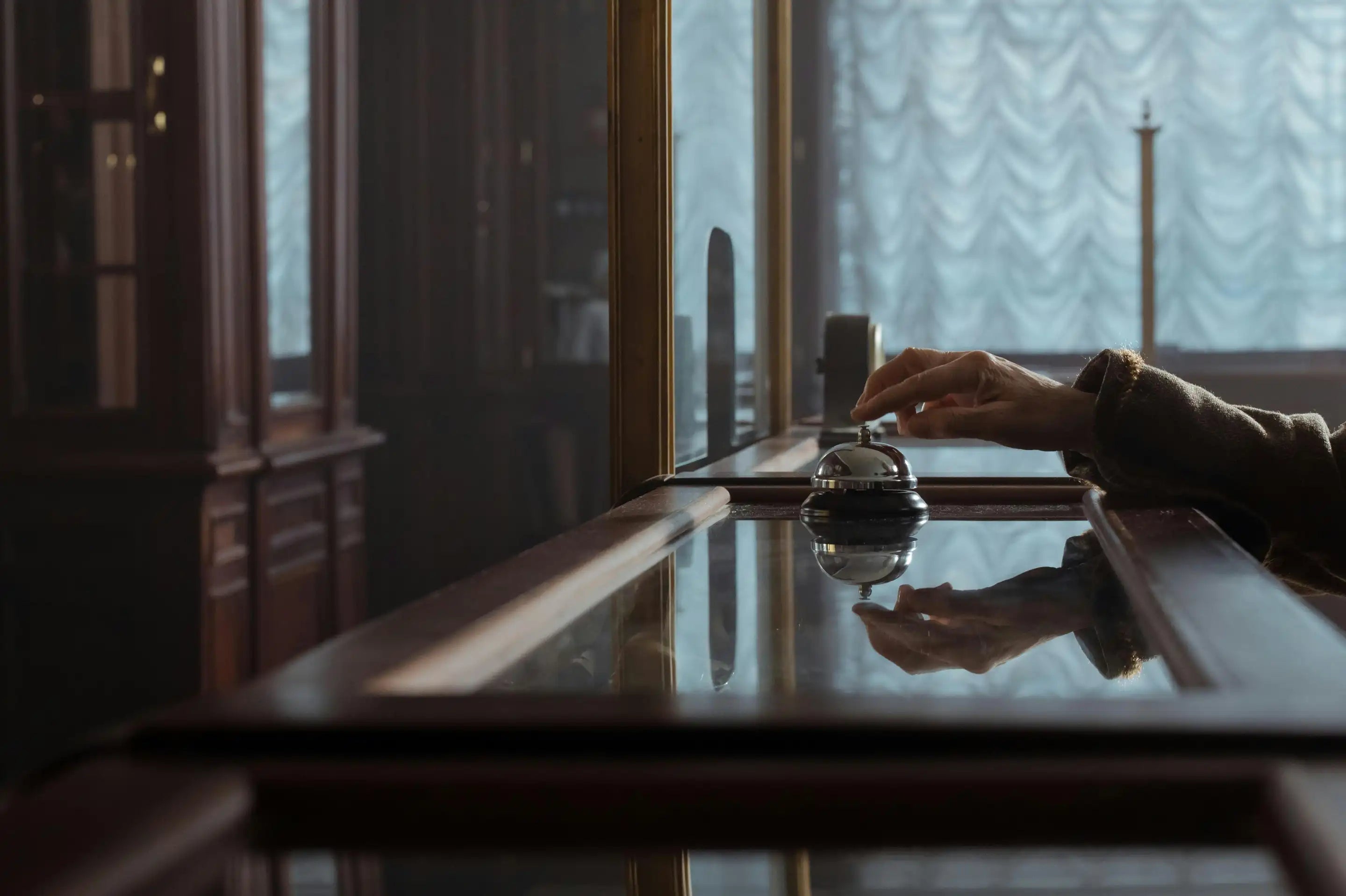 En hånd trykker på en bordklokke i en klassisk reception – symbol på Aedels personlige kundeservice og menneskelig kontakt.